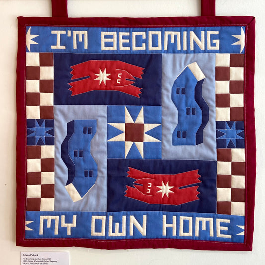 Quilt with text 'I'm becoming my own home' and star designs on a red border.