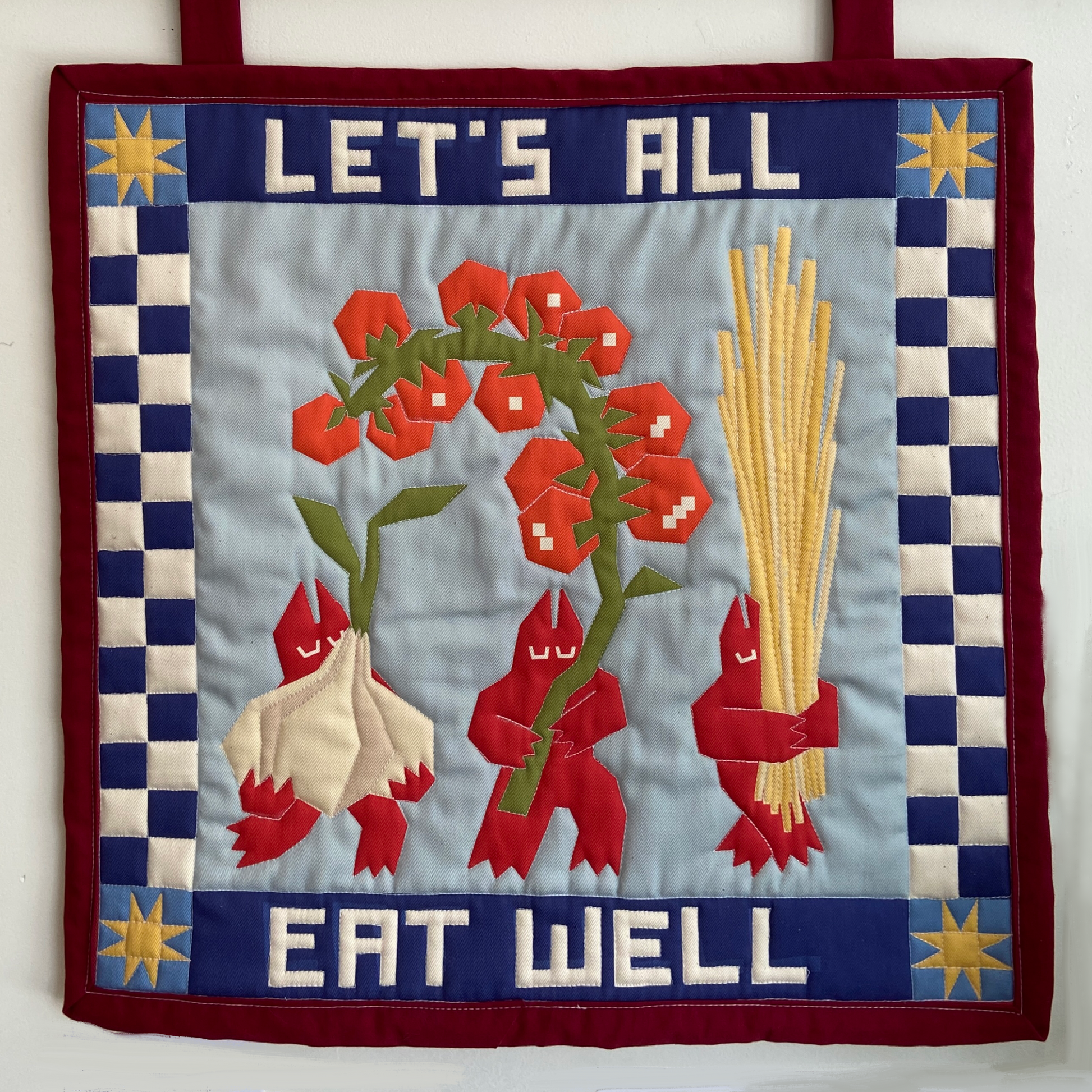 Quilt with tomato, garlic, and pasta design and 'Let's All Eat Well' text on a blue background